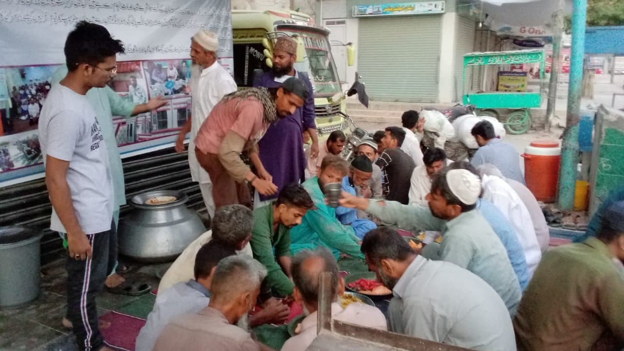 Dozens of people seated on mats eating a hot meal served from large cooking pots at the Shaan Welfare Dastarkhwan in Orangi Town, Karachi, May 2021.